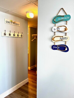 A hallway with a coat rack, a sign that says "GONE TO THE BEACH," and a wall decoration with the words "THE BEACH Is My happy place." - Angelfish Haven - Sands Oceanfront Luxury Condo (Myrtle Beach)