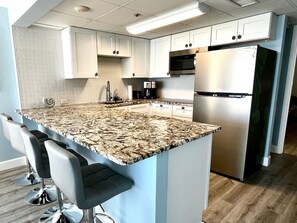 Eine moderne Küche mit weißen Schränken, einem Edelstahl-Kühlschrank, einer eingebauten Mikrowelle und einer Arbeitsplatte aus Granit.