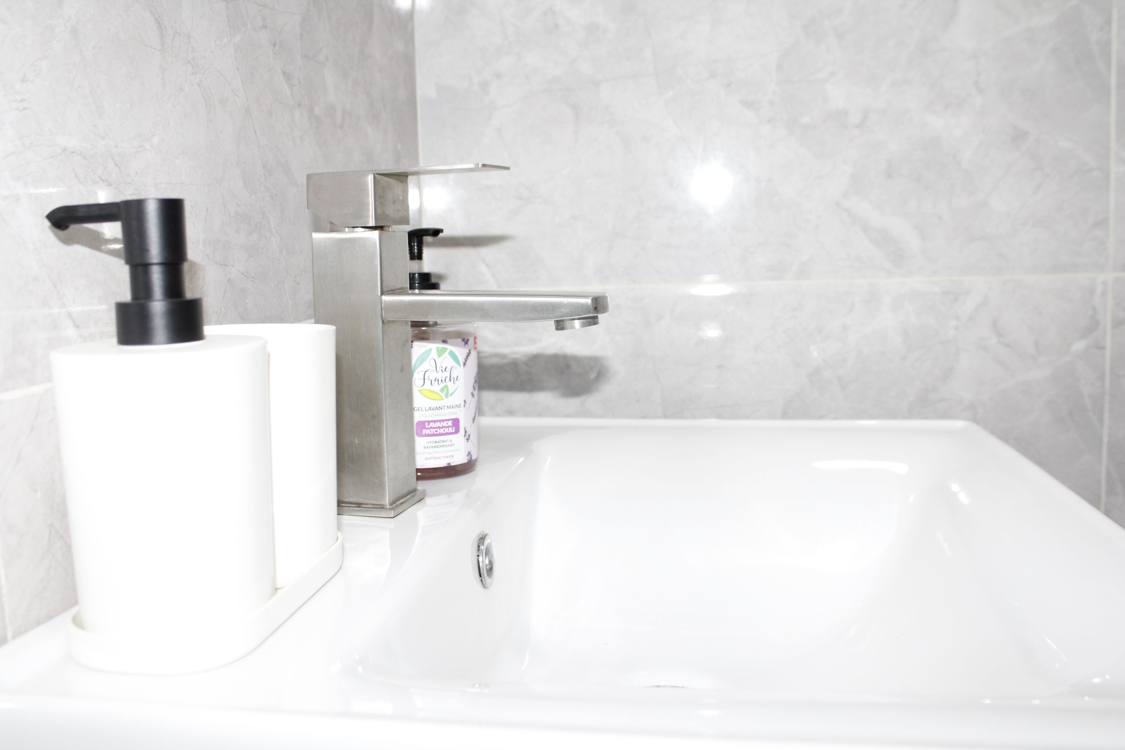 A bathroom with a white sink, a modern faucet, and a soap dispenser.