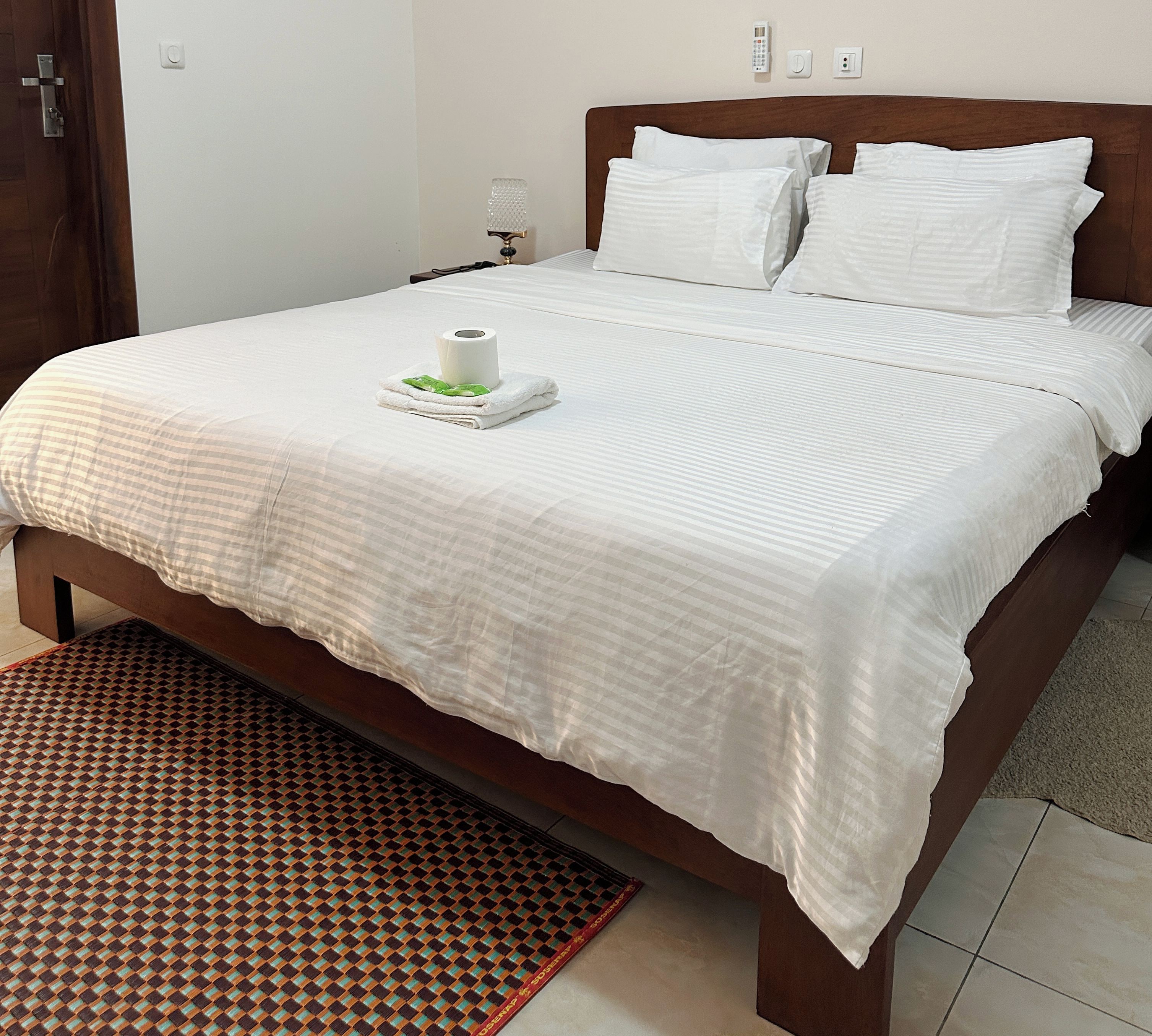 Una cama bien hecha con una colcha blanca, dos almohadas y una toalla enrollada con una hoja verde.