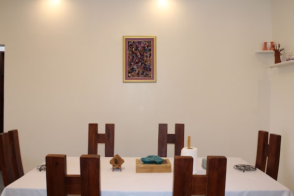 A dining area with a table set for four, wooden chairs, a framed abstract painting on the wall, and a small decorative item on the table. - Residence Nehemie (Abidjan)