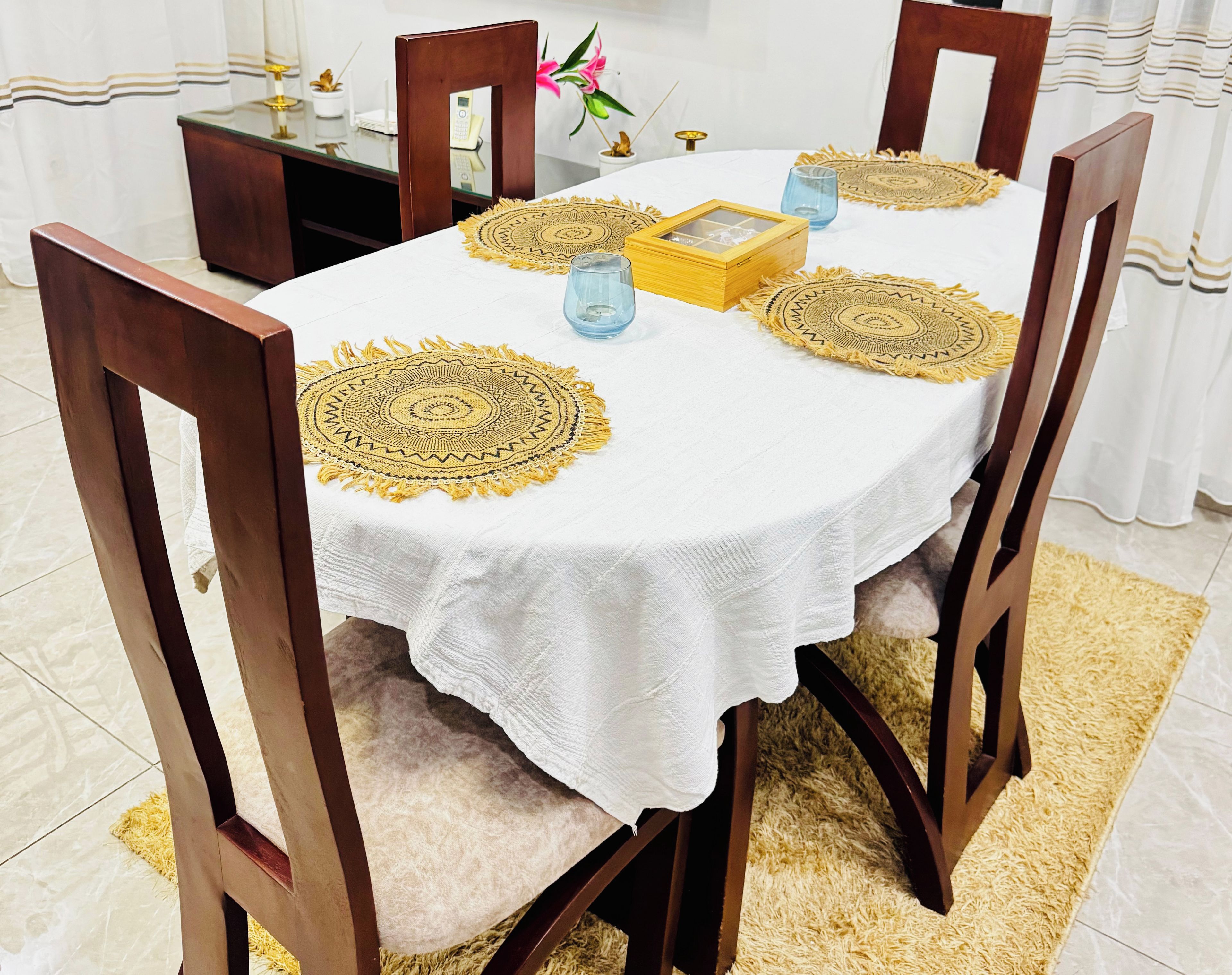 A round dining table with a white tablecloth, surrounded by wooden chairs.