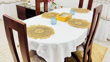 A round dining table with a white tablecloth, surrounded by wooden chairs.