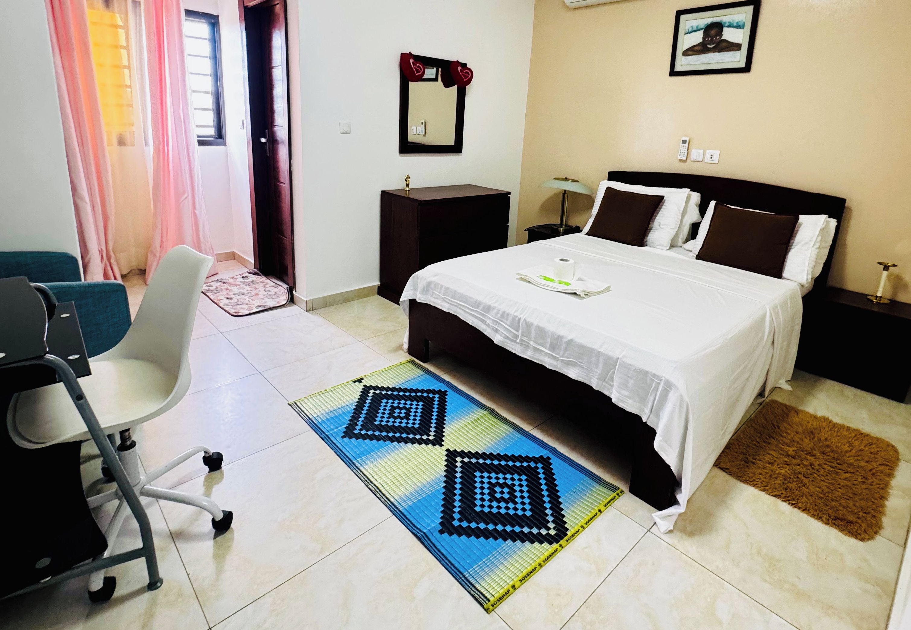 Ein Hotelzimmer mit Bett, Nachttischen, einem Schreibtisch, einem Sessel und einem Teppich mit Muster sowie einer Tür.