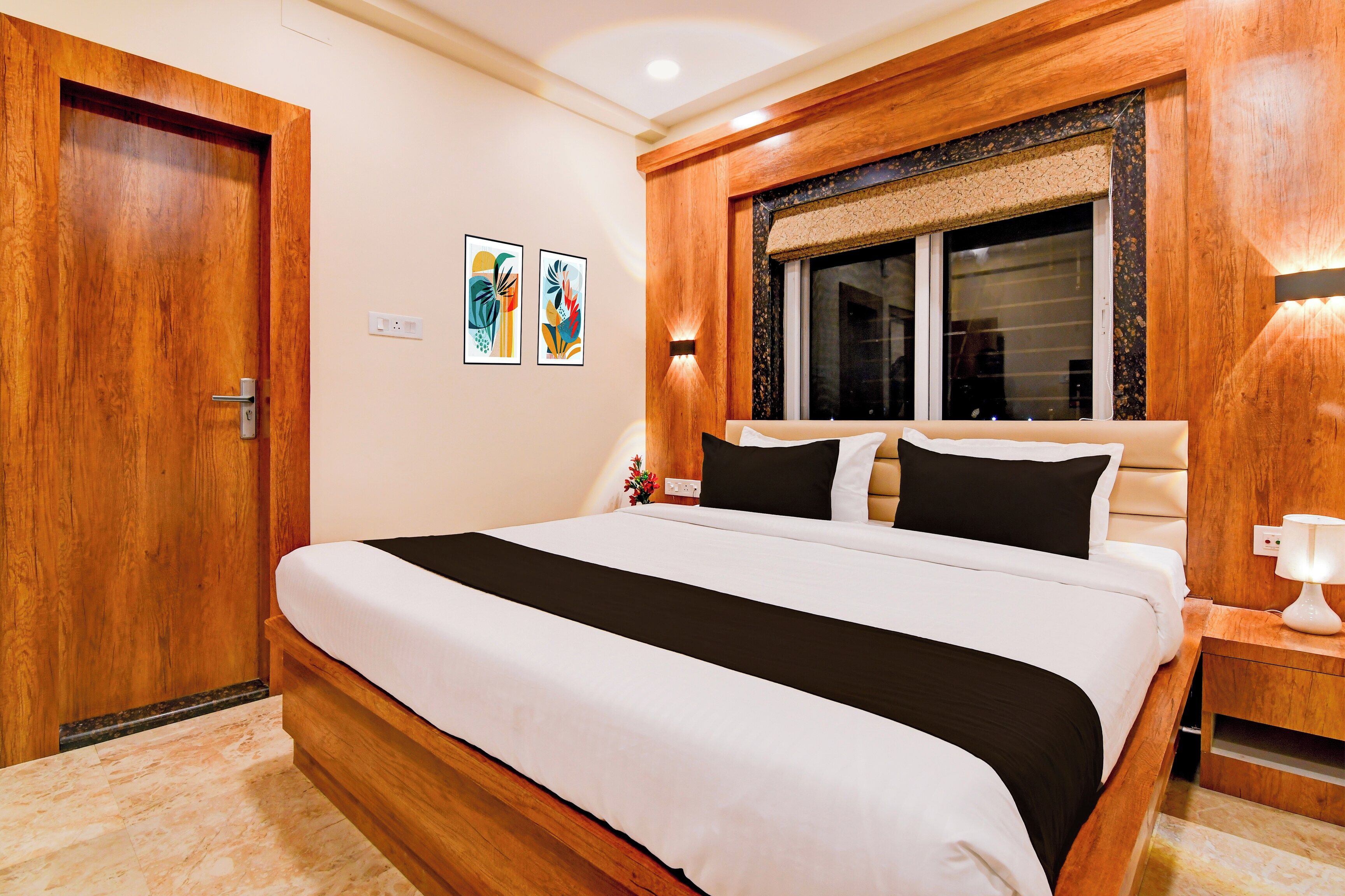 Ein Hotelzimmer mit einem Bett, einem Holzkopfteil, einem Nachttisch mit Lampe und zwei an der Wand befestigten Kunstwerken.