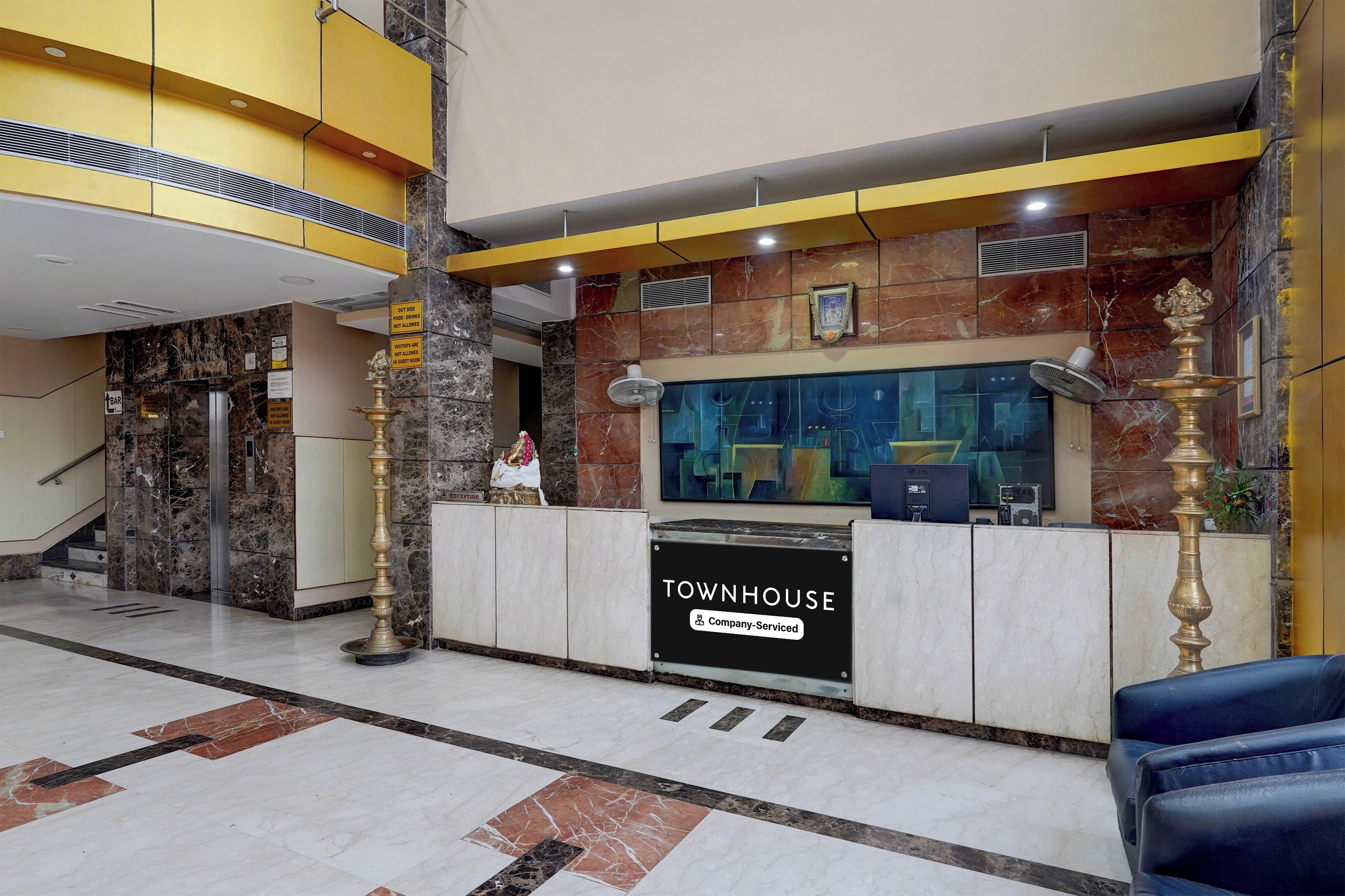 Un mostrador de recepción con la etiqueta 'TOWNHOUSE', un suelo de mármol y una escalera al fondo.