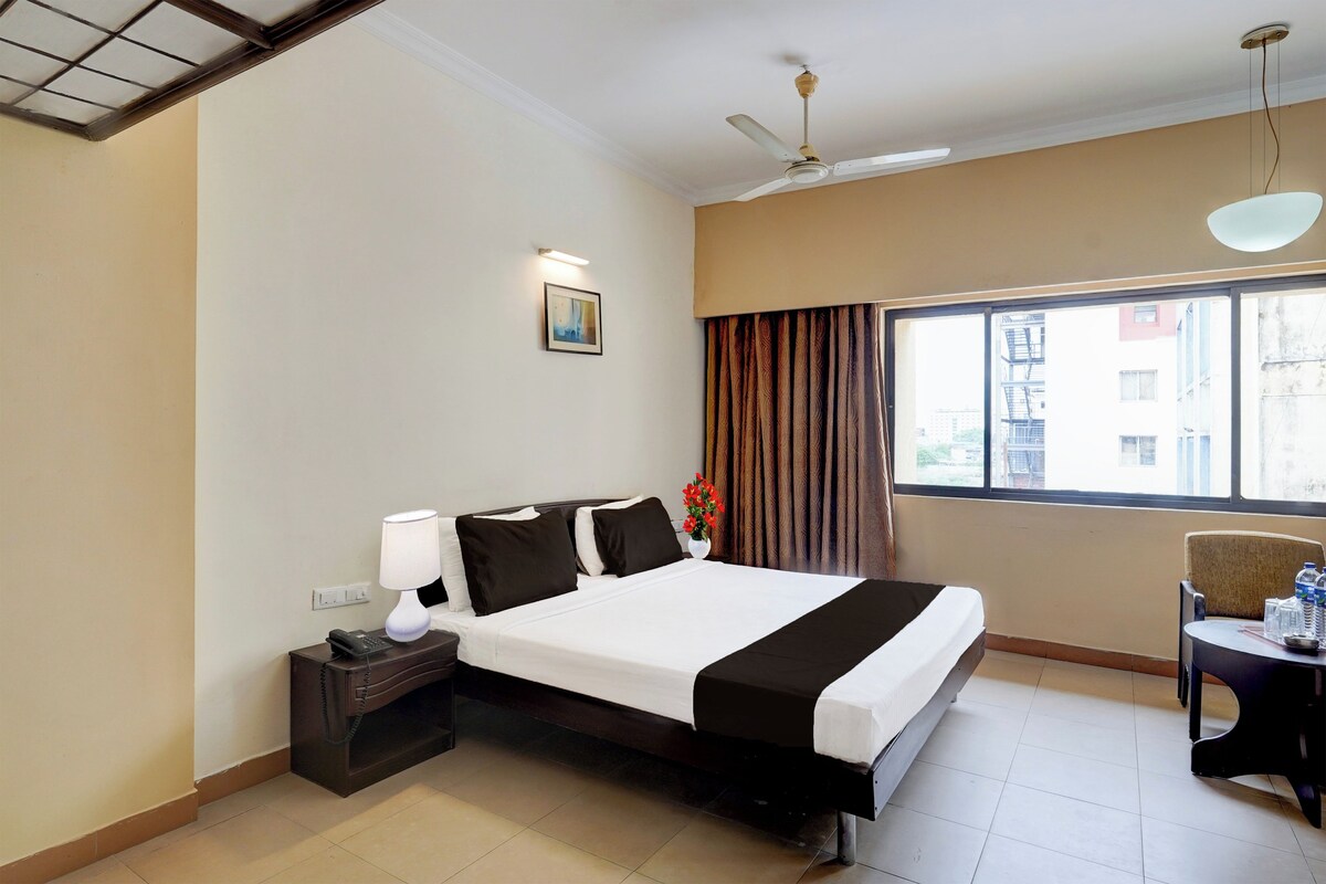 Habitación de hotel con cama, lámpara de noche, mesita de noche y ventana con cortinas.