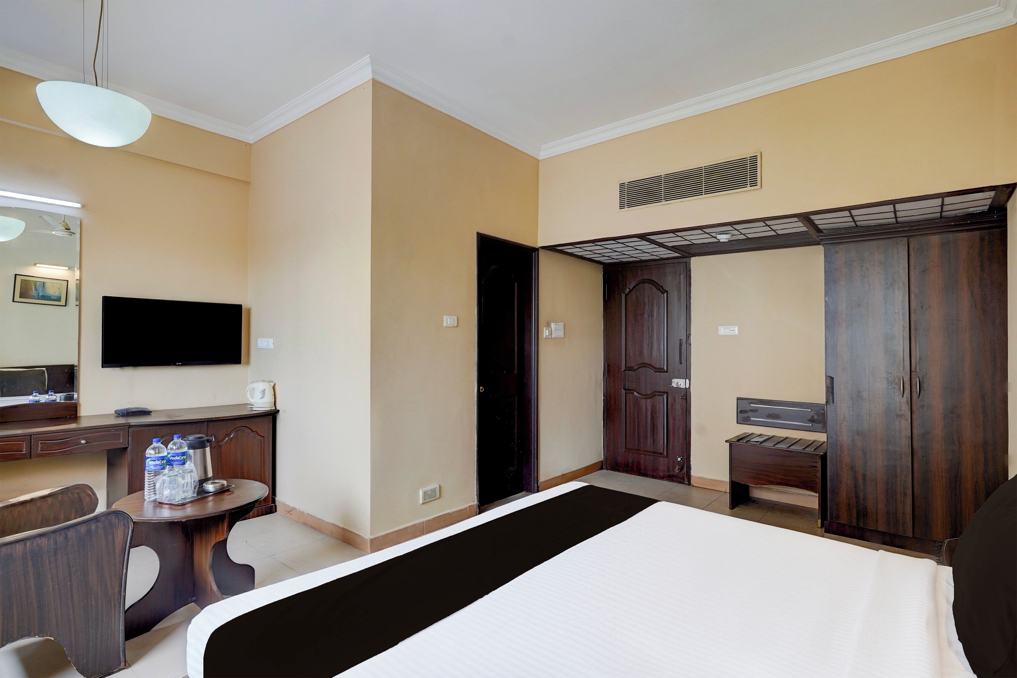 Quarto de hotel com cama, escrivaninha, televisão, guarda-roupa e banheiro.