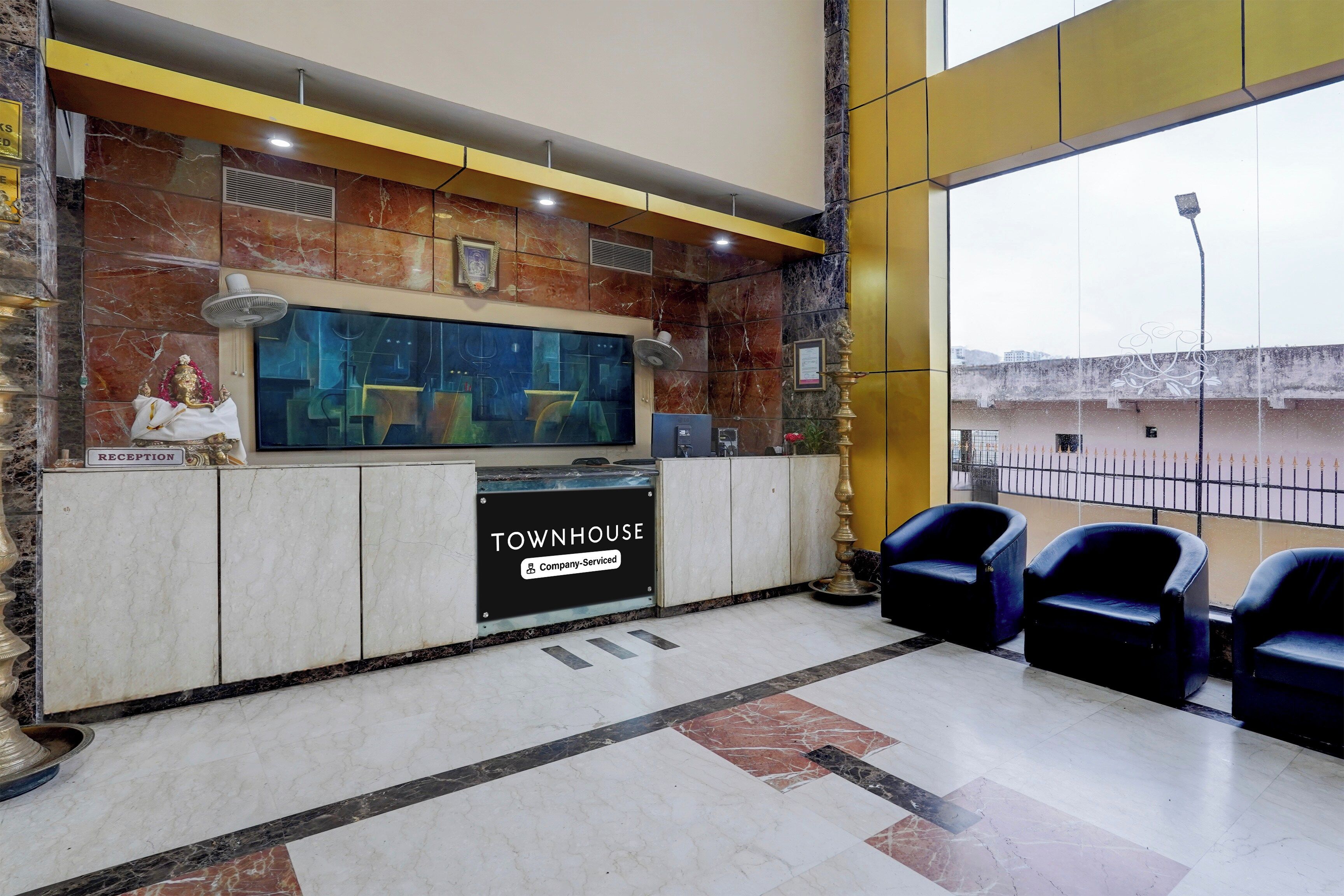 Uma área de recepção com parede de mármore, televisão e placa indicando 'TOWNHOUSE Company-Serviced'.