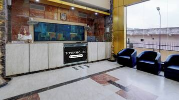 Uma área de recepção com parede de mármore, televisão e placa indicando 'TOWNHOUSE Company-Serviced'.