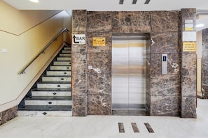 Ascensor de hotel con pared de mármol, barandilla y cartel que indica el bar en el primer piso.