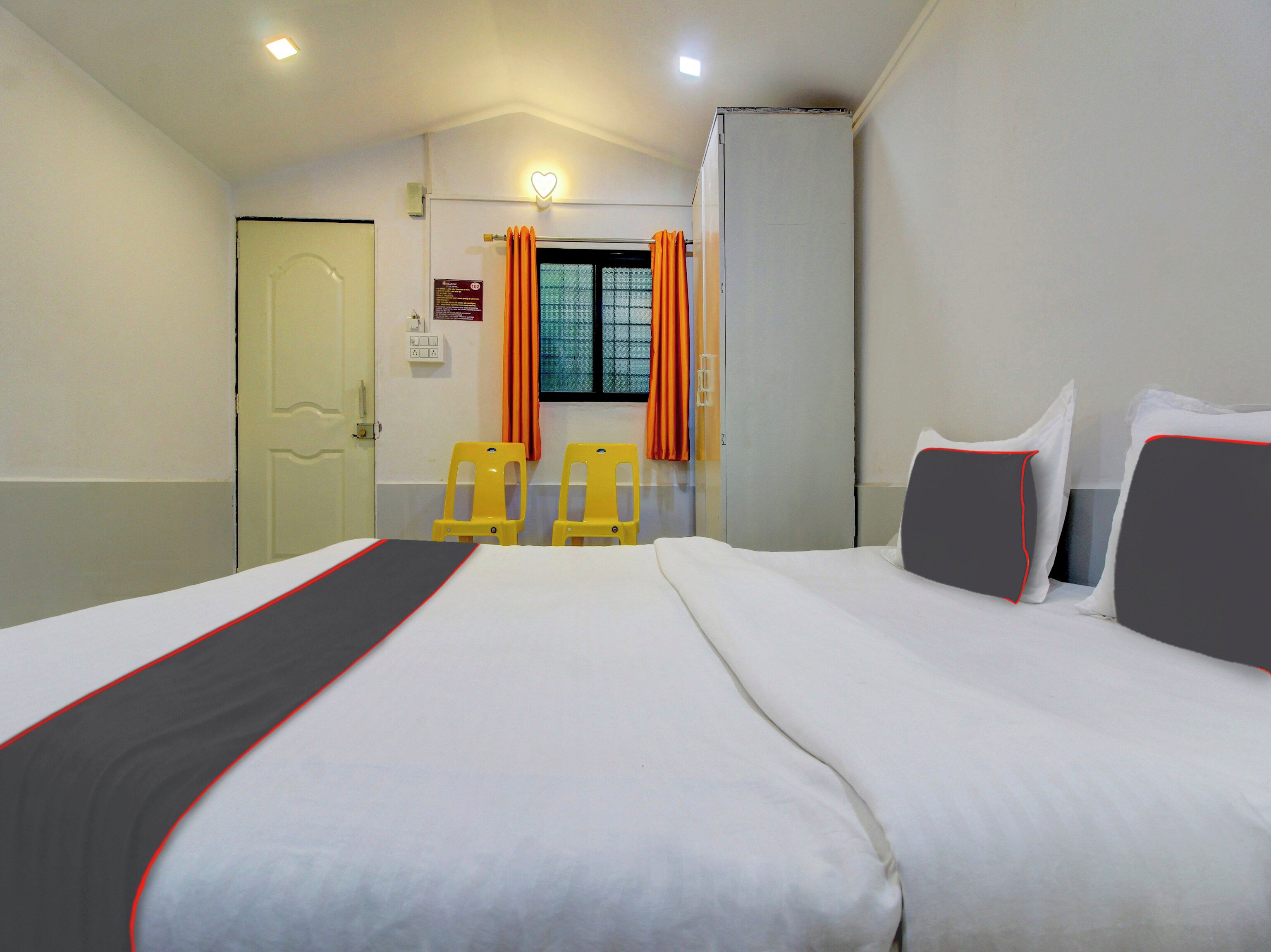 Una habitación de hotel con una cama, dos sillas, un armario y una ventana con cortinas.