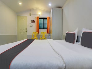 Una habitación de hotel con una cama, dos sillas, un armario y una ventana con cortinas.