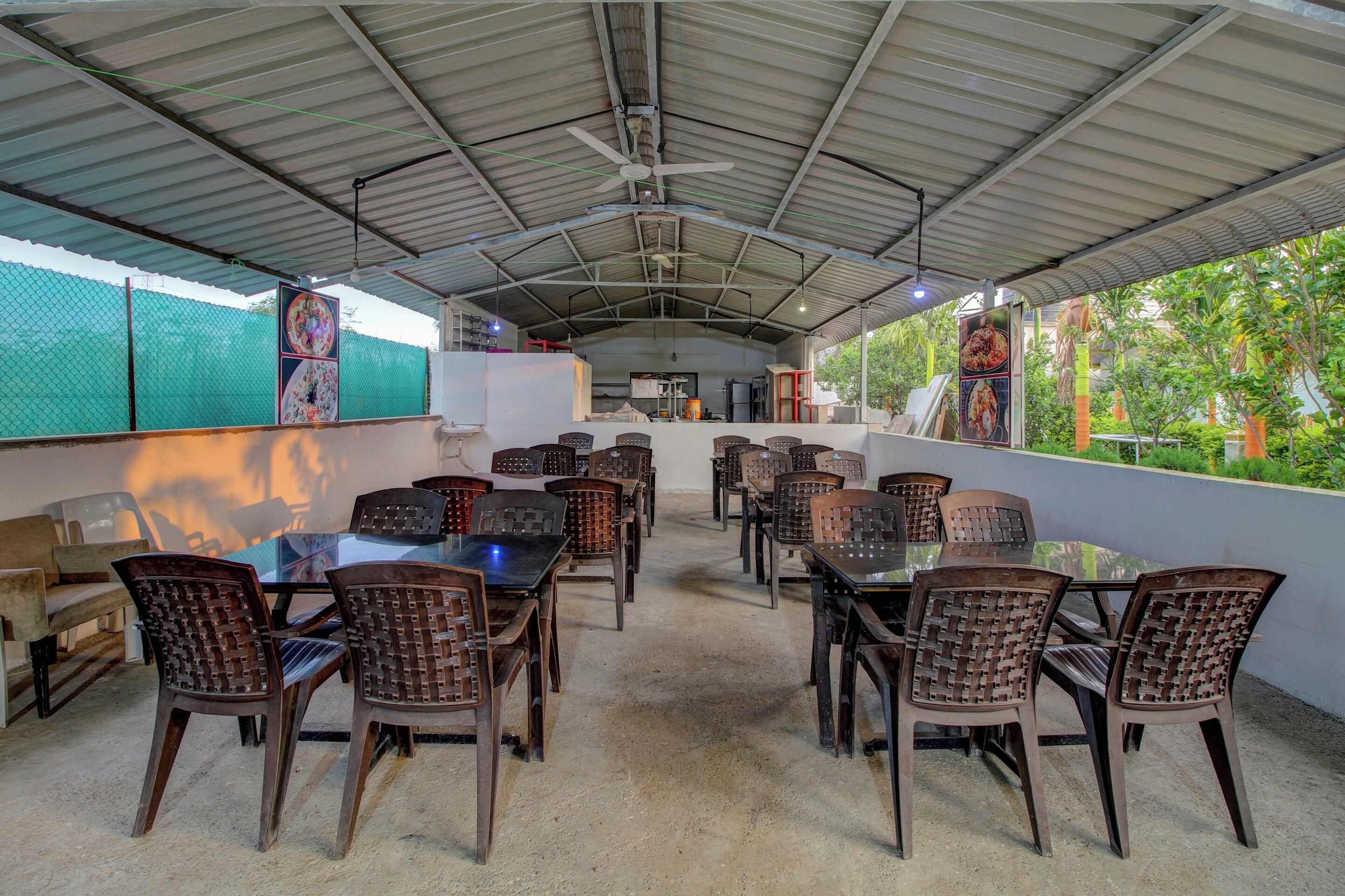 An outdoor dining area with tables and chairs, a ceiling fan, and a view of greenery.