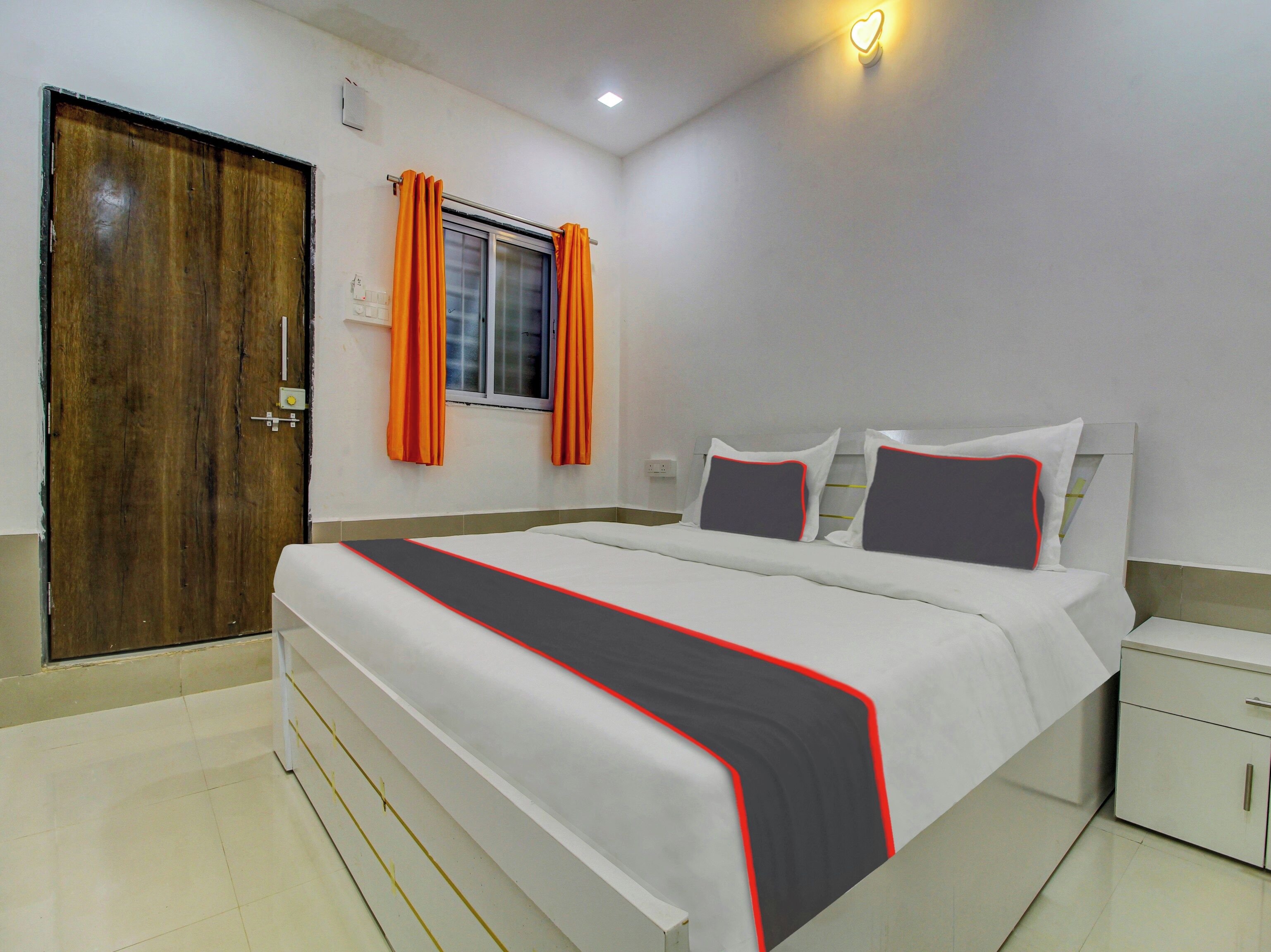 Una habitación de hotel con cama, mesita de noche, armario, ventana con cortinas y puerta.