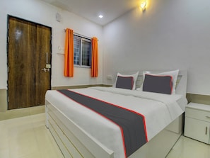 A hotel room with a bed, a nightstand, a wardrobe, a window with curtains, and a door. - Hotel O Homely Stays Resort (Pune)