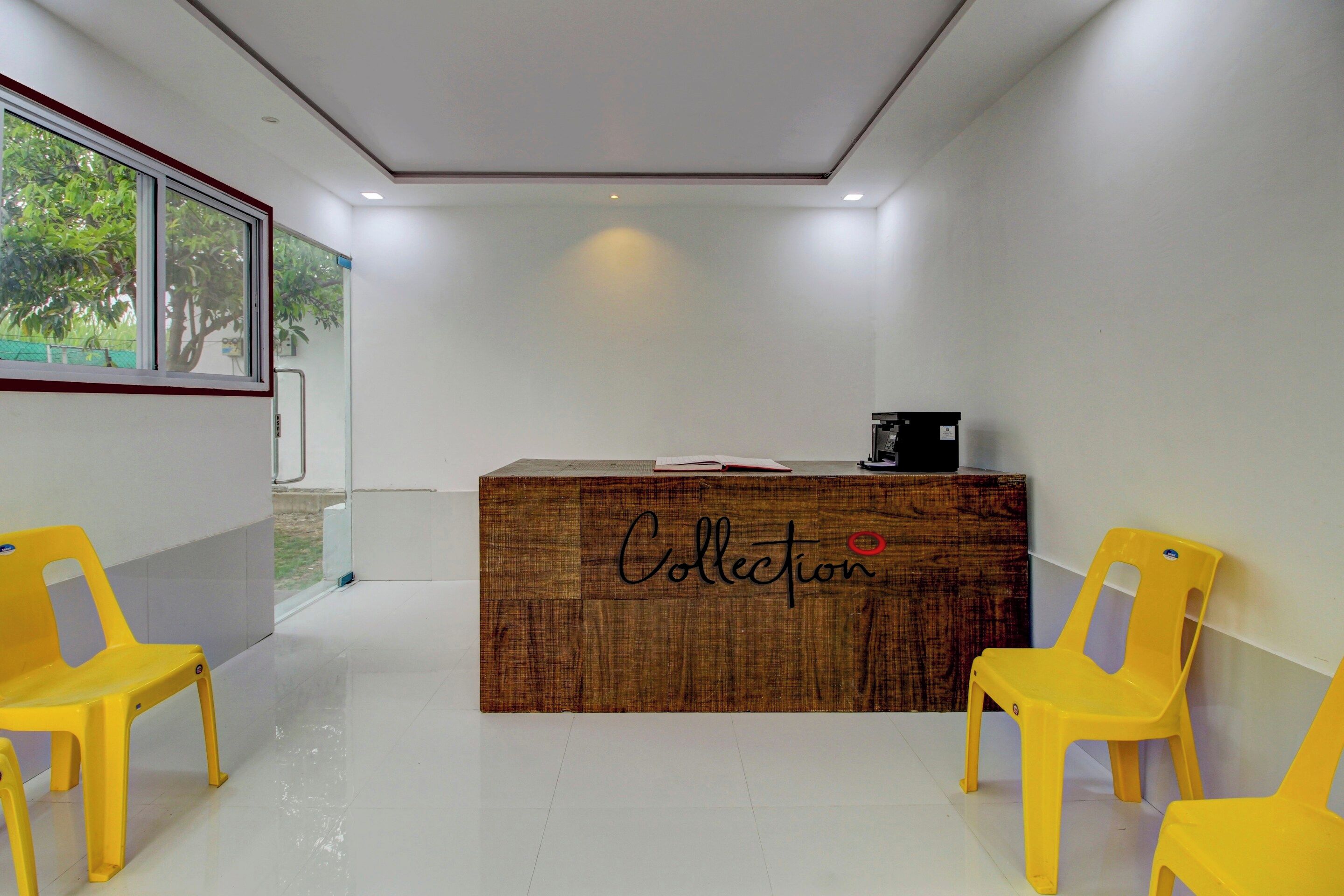 A reception desk with a wooden finish and the word 'Collection' on it, flanked by two yellow chairs.