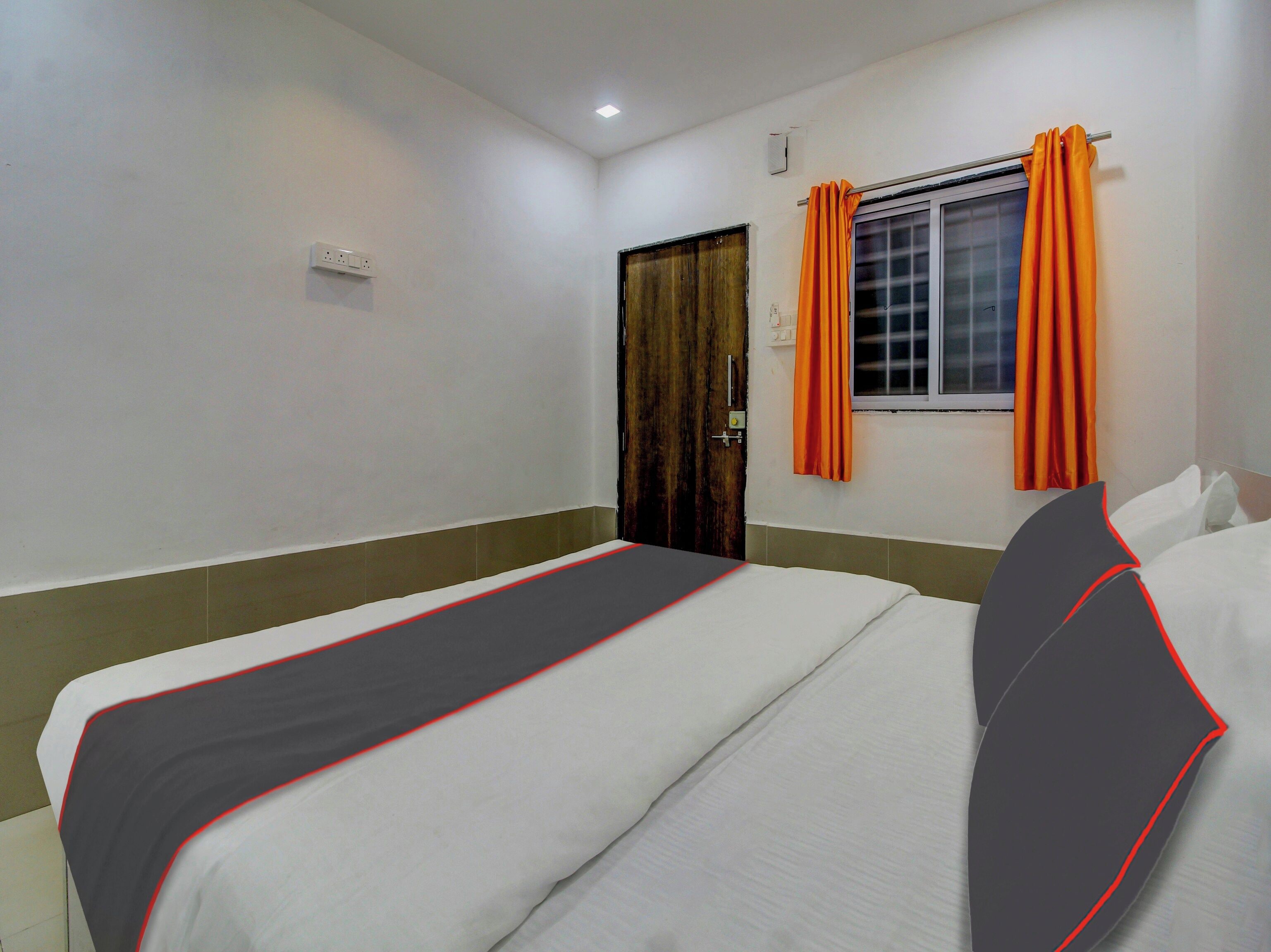 Habitación de hotel con una cama individual, una ventana con cortinas, una puerta y un interruptor de luz en la pared.