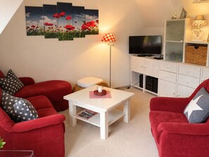 Ein Wohnzimmer mit roten Sofas, einem weißen Couchtisch, einem Flachbildfernseher und einer Wandleuchte.