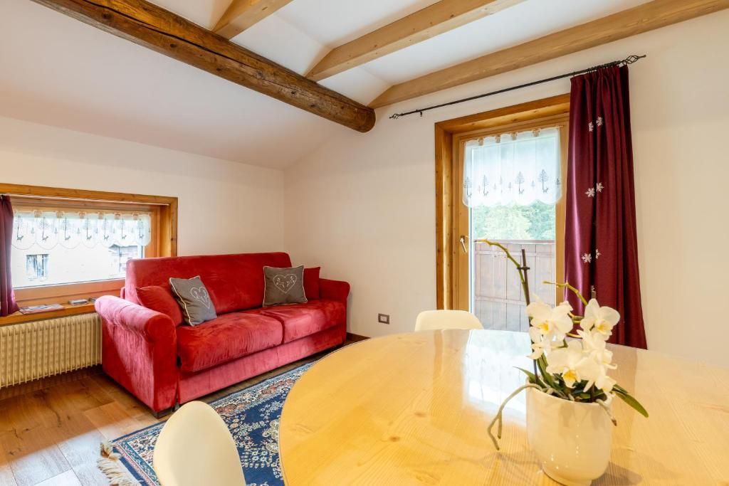 Una habitación con un sofá rojo, una mesa de madera redonda y una ventana con cortinas.