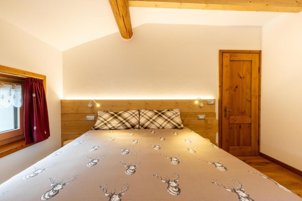 Un dormitorio con cama, cabecera de madera, ventana con cortinas, una puerta y luces fijadas en la pared.