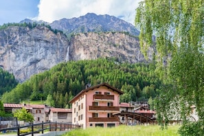 A mountain resort with a building featuring balconies and a view of a waterfall.