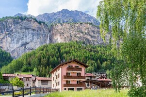 Un complejo turístico de montaña con un edificio que tiene balcones y vista a una cascada.