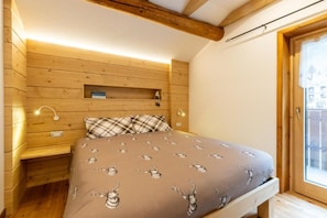 A bedroom with a wooden headboard, a bed with a patterned bedspread, a bedside table, and a small shelf.