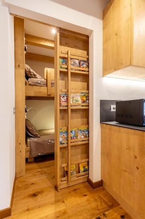 A wooden closet with shelves containing books and a bed with a blanket.