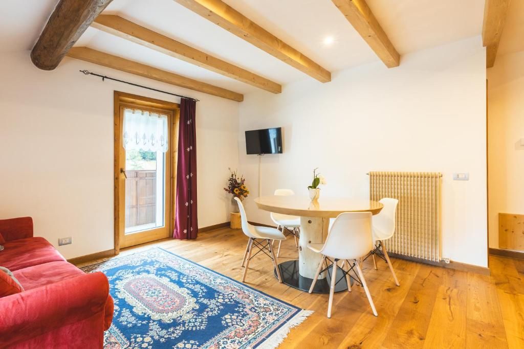 Een kamer met een rode bank, een ronde eettafel met stoelen, een aan de muur bevestigde televisie en een radiator.