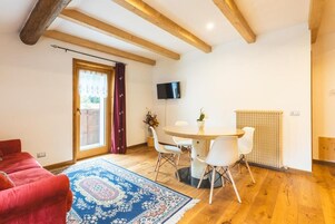 A room with a red sofa, a round dining table with chairs, a TV mounted on the wall, and a radiator.