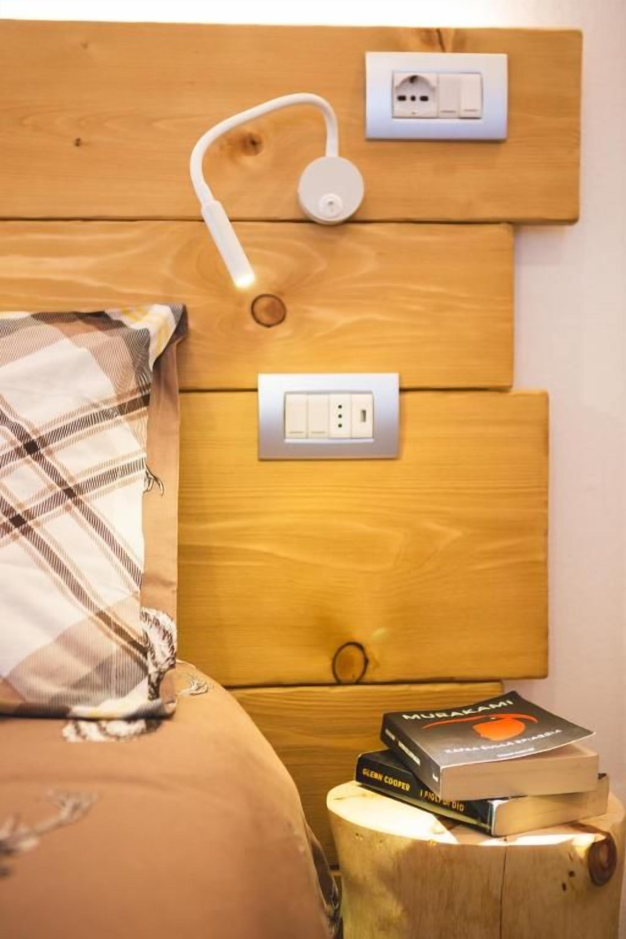 Una testiera in legno con una presa di corrente e una spina, un comodino con un libro e un cuscino a quadri.