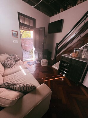 Un salon avec un canapé, un téléviseur fixé au mur, un escalier et une porte donnant sur l’extérieur.
