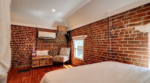 A bedroom with a brick wall, a bed, a chair, a small table, and a window. - Cozy one bedroom private historic apt (Norfolk)