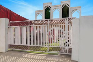 Una entrada cerrada con una valla metálica blanca y un toldo rojo al fondo.