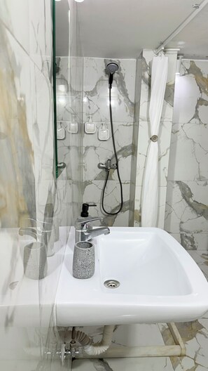 A bathroom with a white sink, a handheld showerhead, and a glass shower enclosure. - Exarcheia secret cozy apartment (Athina)
