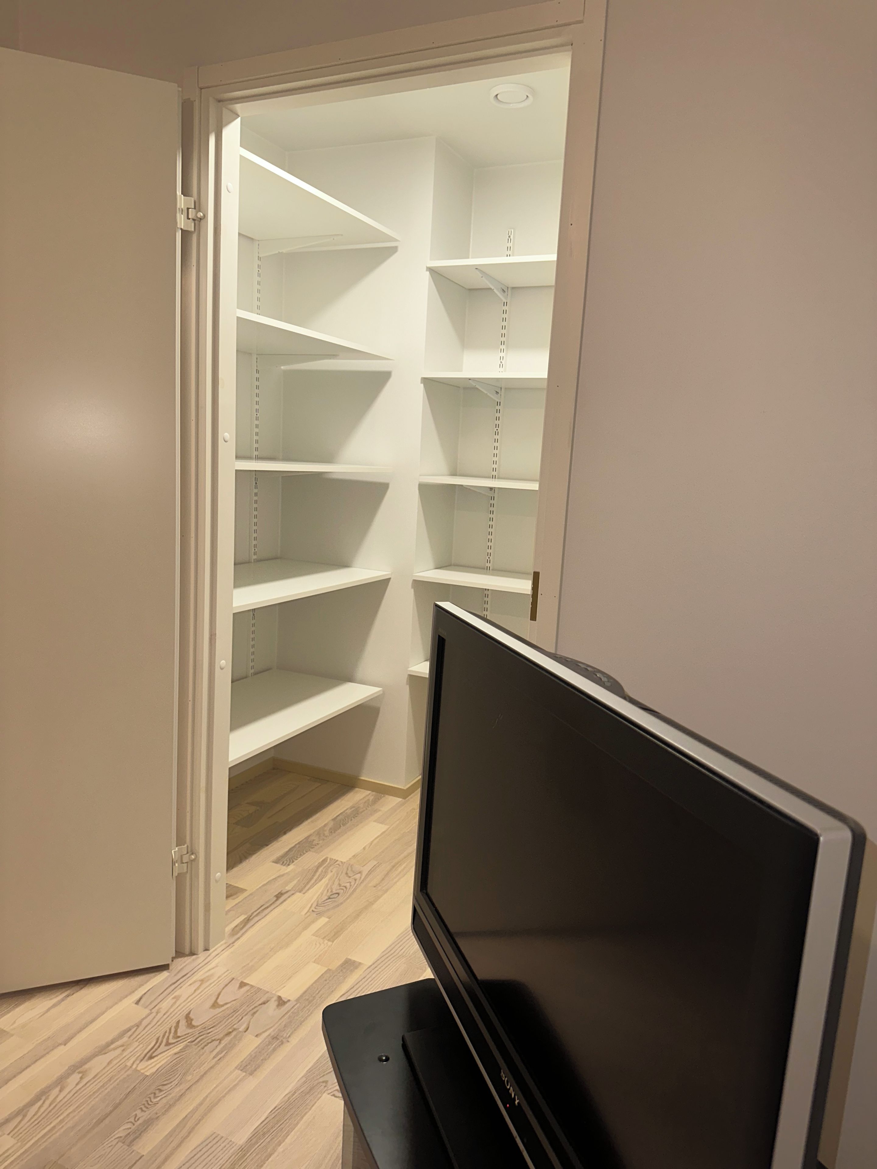 Ein begehbarer Kleiderschrank mit mehreren Regalen und einem Flachbildfernseher im Vordergrund.