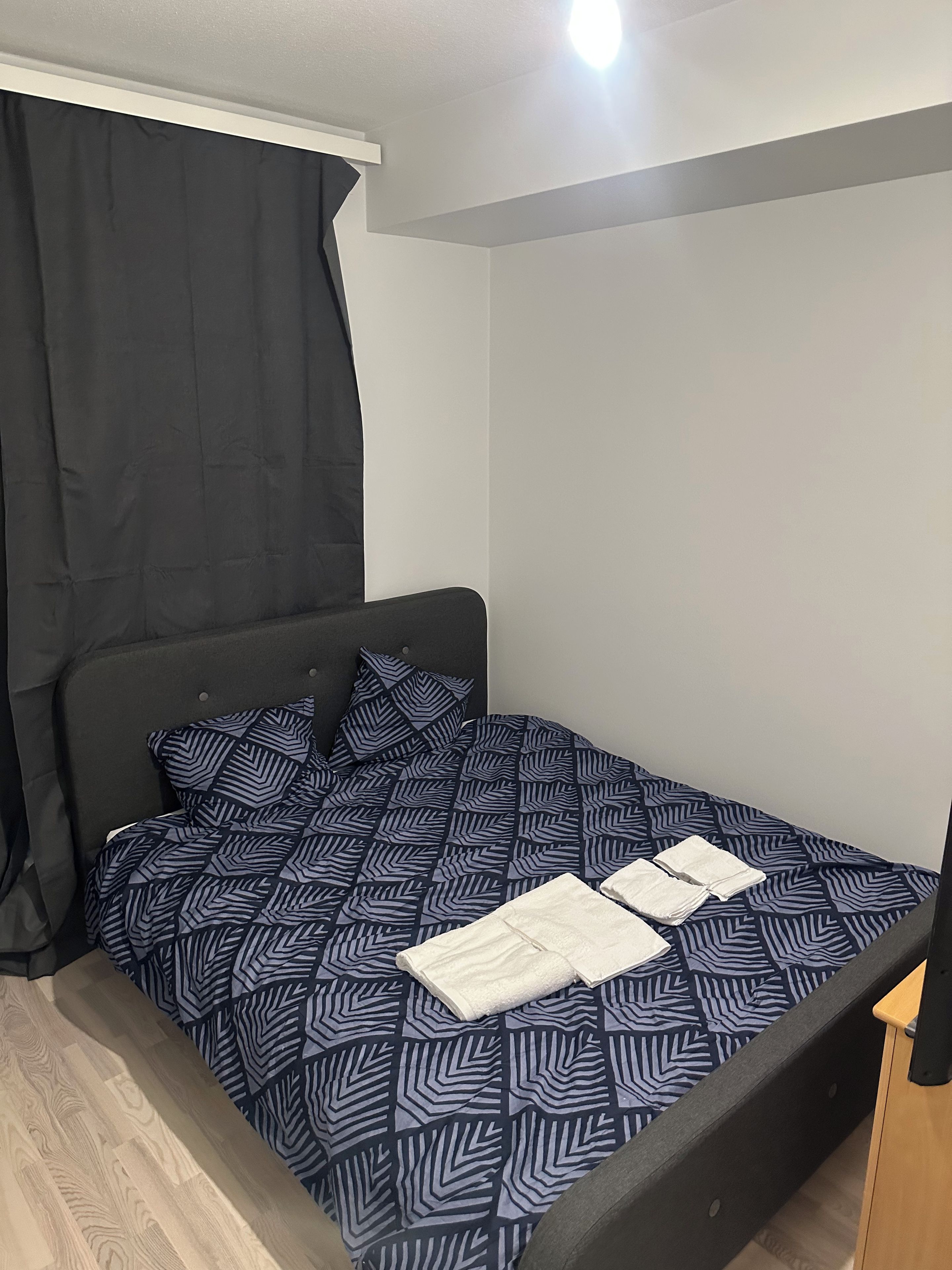 A single bed with a patterned bedspread, a headboard, and a bedside table with a lamp.