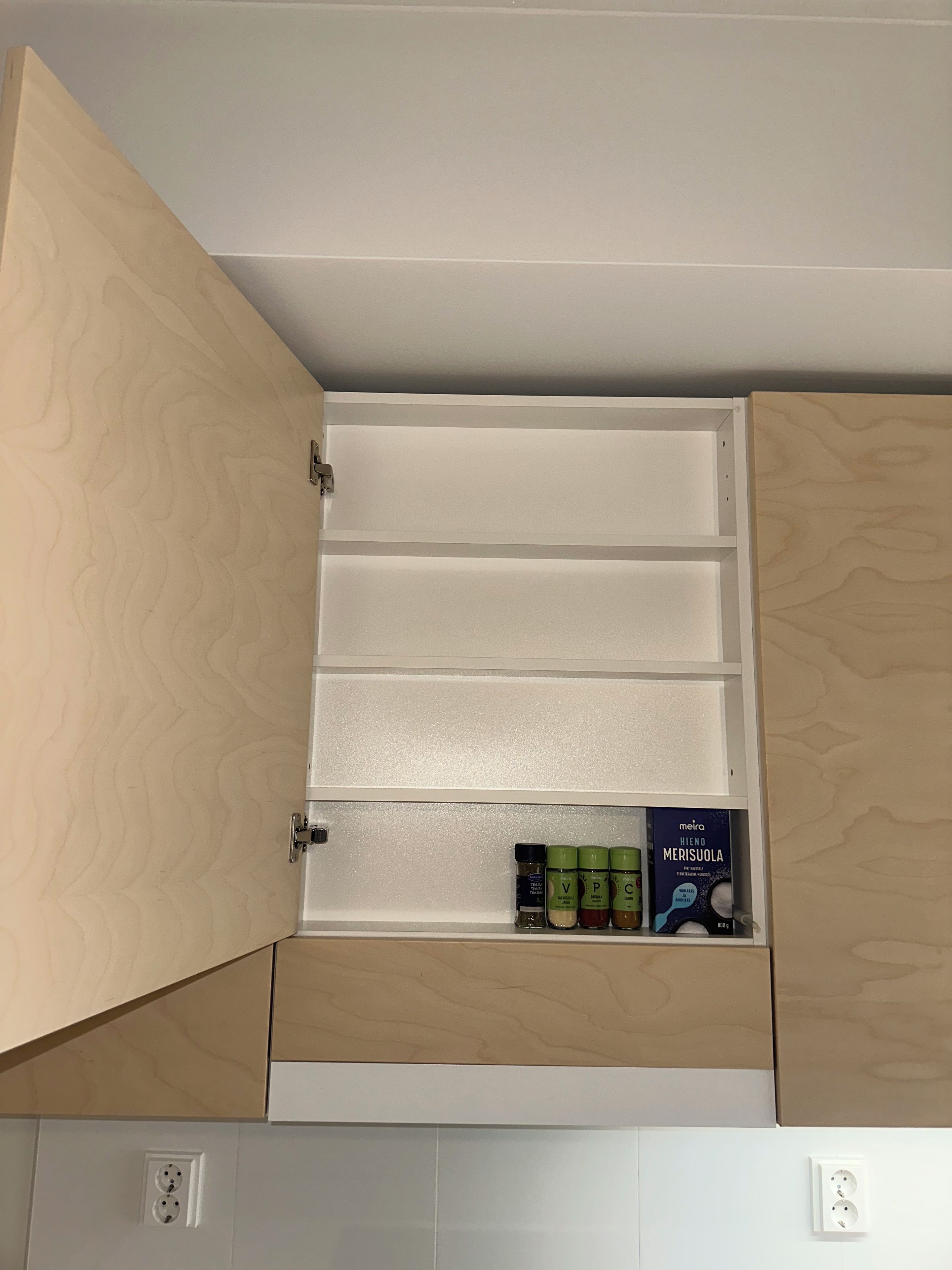 A kitchen cabinet with multiple compartments, including a section with spice jars and a box labeled 'meira'.