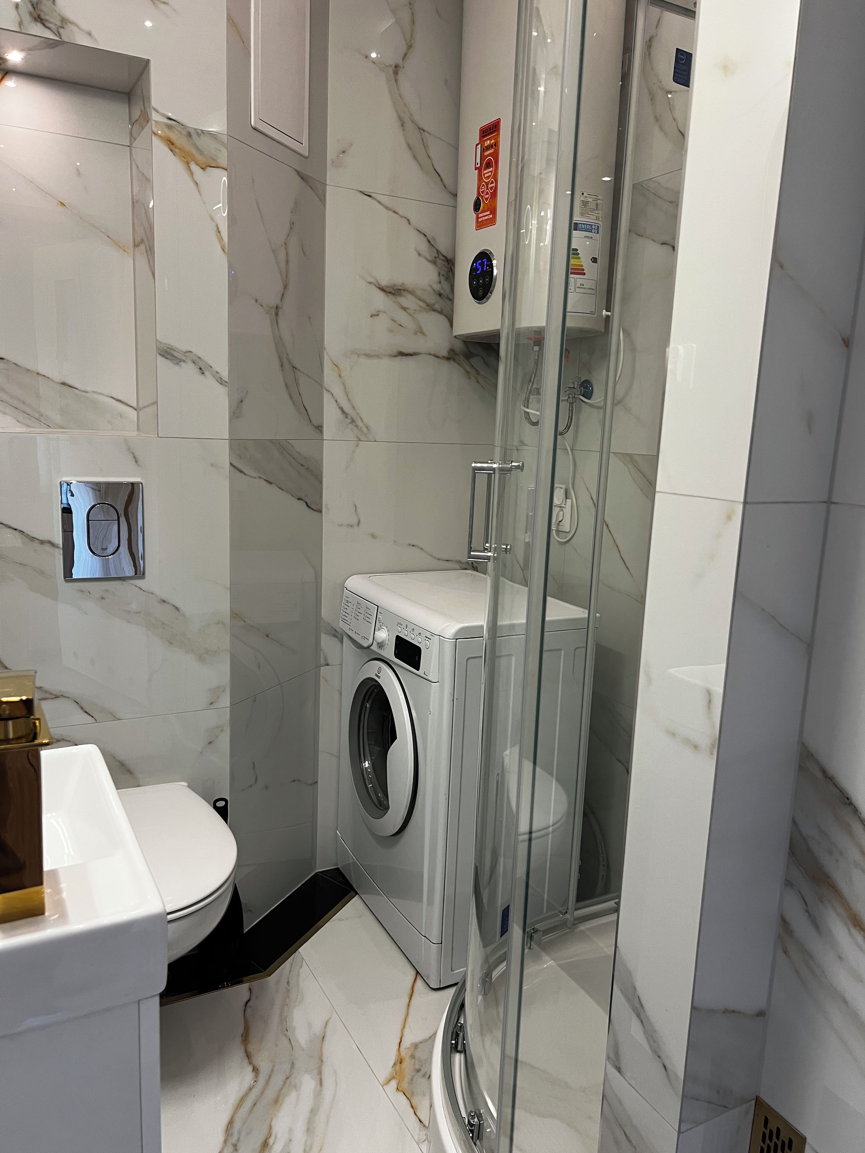 A modern bathroom with a glass-enclosed shower, a built-in washing machine, and a toilet.