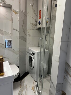 Ein modernes Badezimmer mit einer gläsernen Duschkabine, einer integrierten Waschmaschine und einer Toilette.