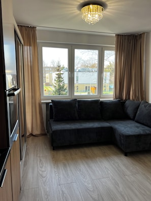 Ein modernes Wohnzimmer mit einer Eckcouch, einer Chandelieber und Blick ins Freie.