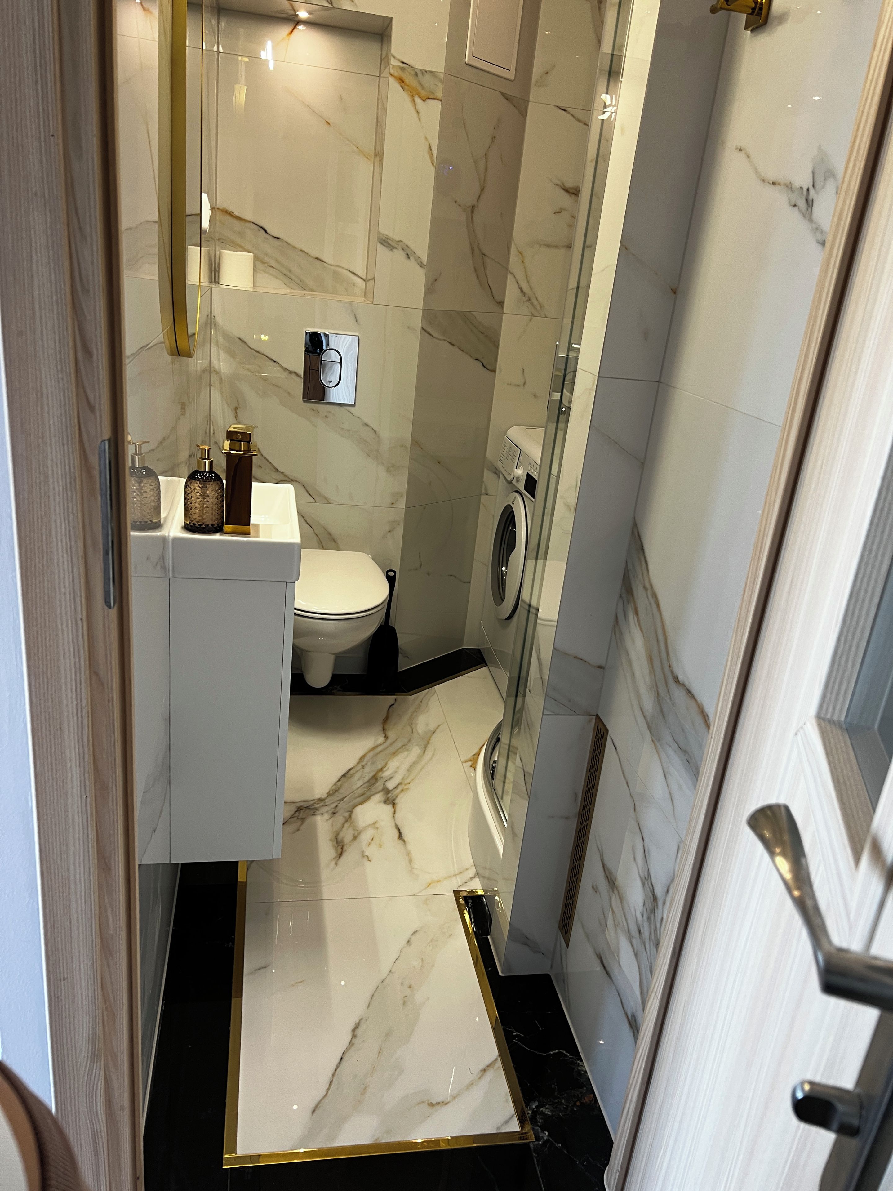 A bathroom with a toilet, washing machine, and a glass-enclosed shower area.