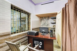 A hotel room with a desk, a chair, a window with bars, and a sign indicating the room is serviced.
