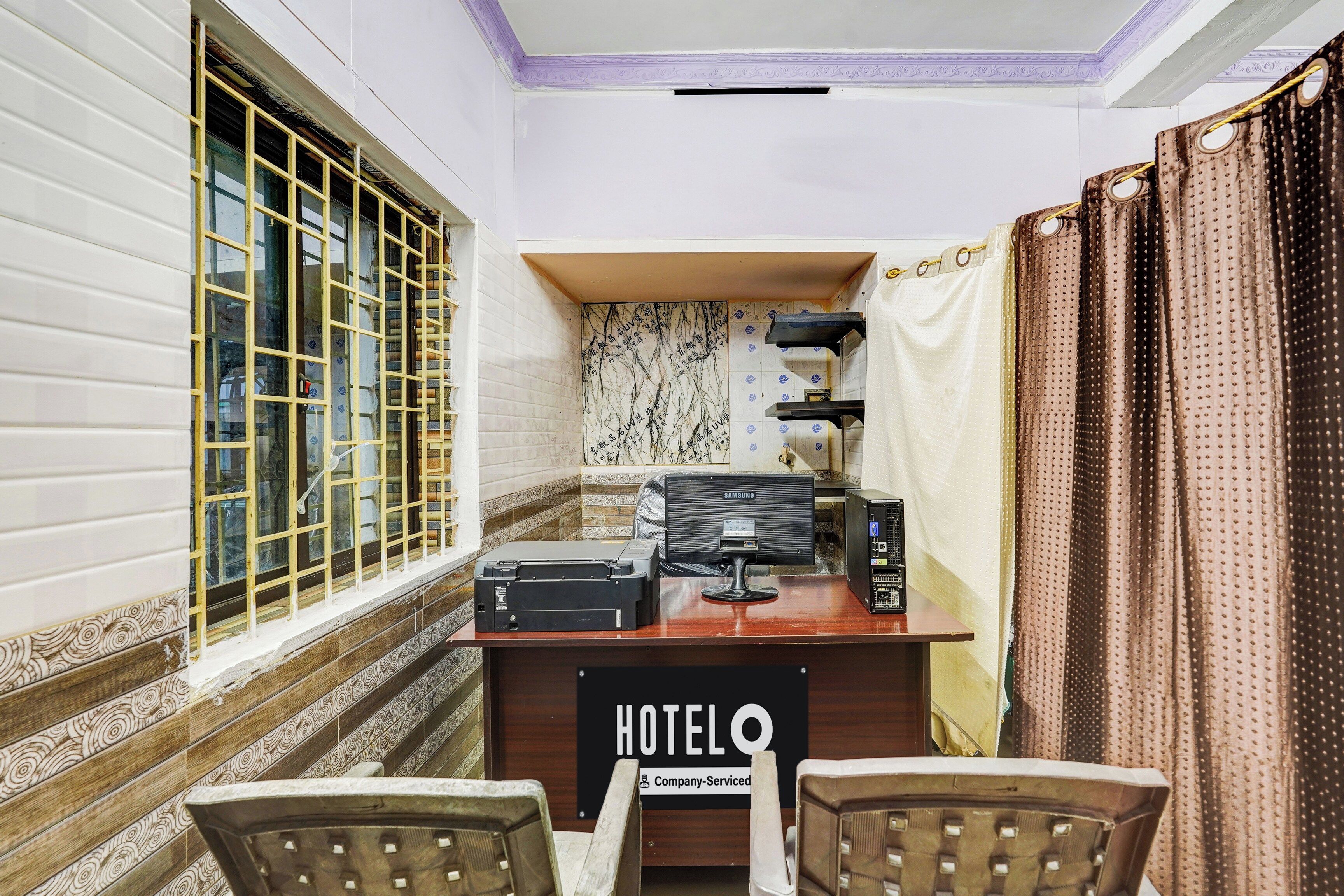 Une chambre d’hôtel équipée d’un bureau, de deux chaises, d’un écran Samsung, d’une imprimante et d’un panneau indiquant qu’il s’agit d’un hôtel proposant des services aux entreprises.