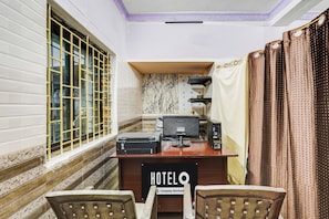 A hotel room with a desk, two chairs, a Samsung monitor, a printer, and a sign indicating it's a company-serviced hotel.