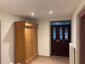 Ein Zimmer mit einem Holfischschrank, einer dunklen Tür mit Glasfeldern und einem Heizkörper.