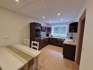 Una cucina compatta con mobili scuri, un'area pranzo con tovaglia a righe e una finestra che offre vista sull'esterno.
