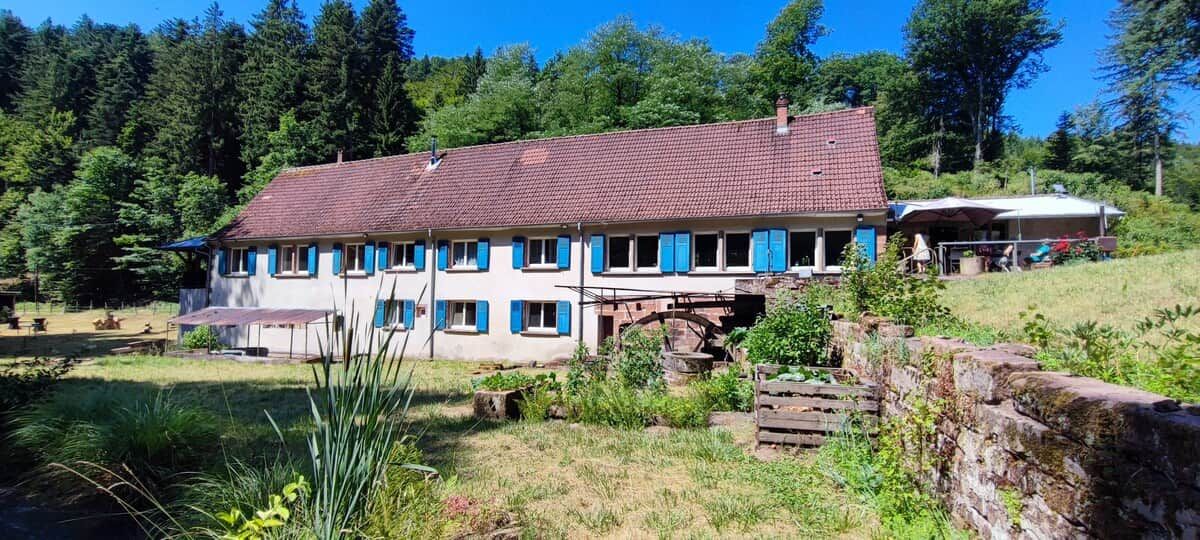 Una casa a due piani con un tetto in tegole rosse, un ponte in pietra e un'area verde davanti.