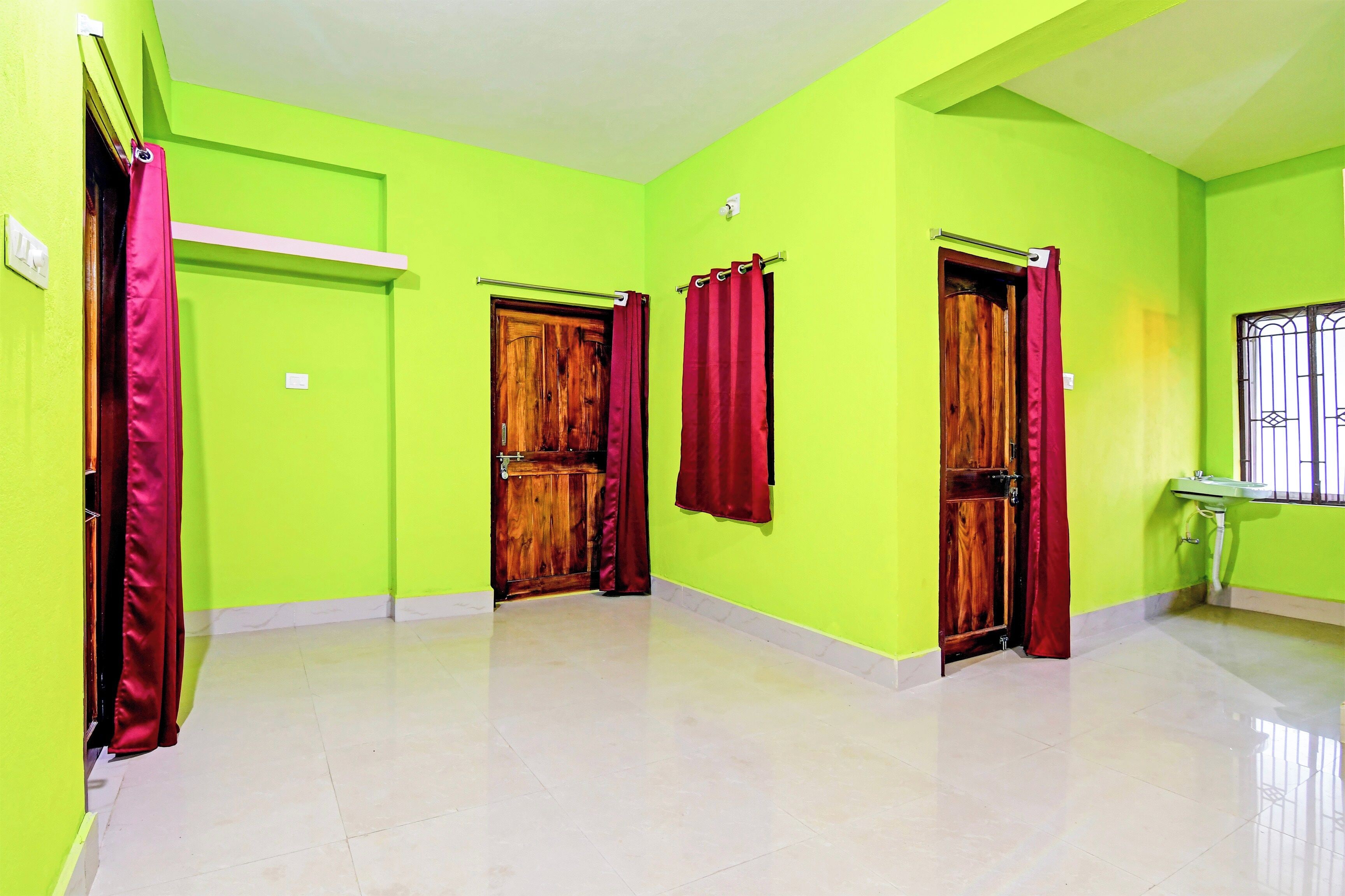 Un pasillo con paredes verdes, puertas de madera y cortinas rojas.